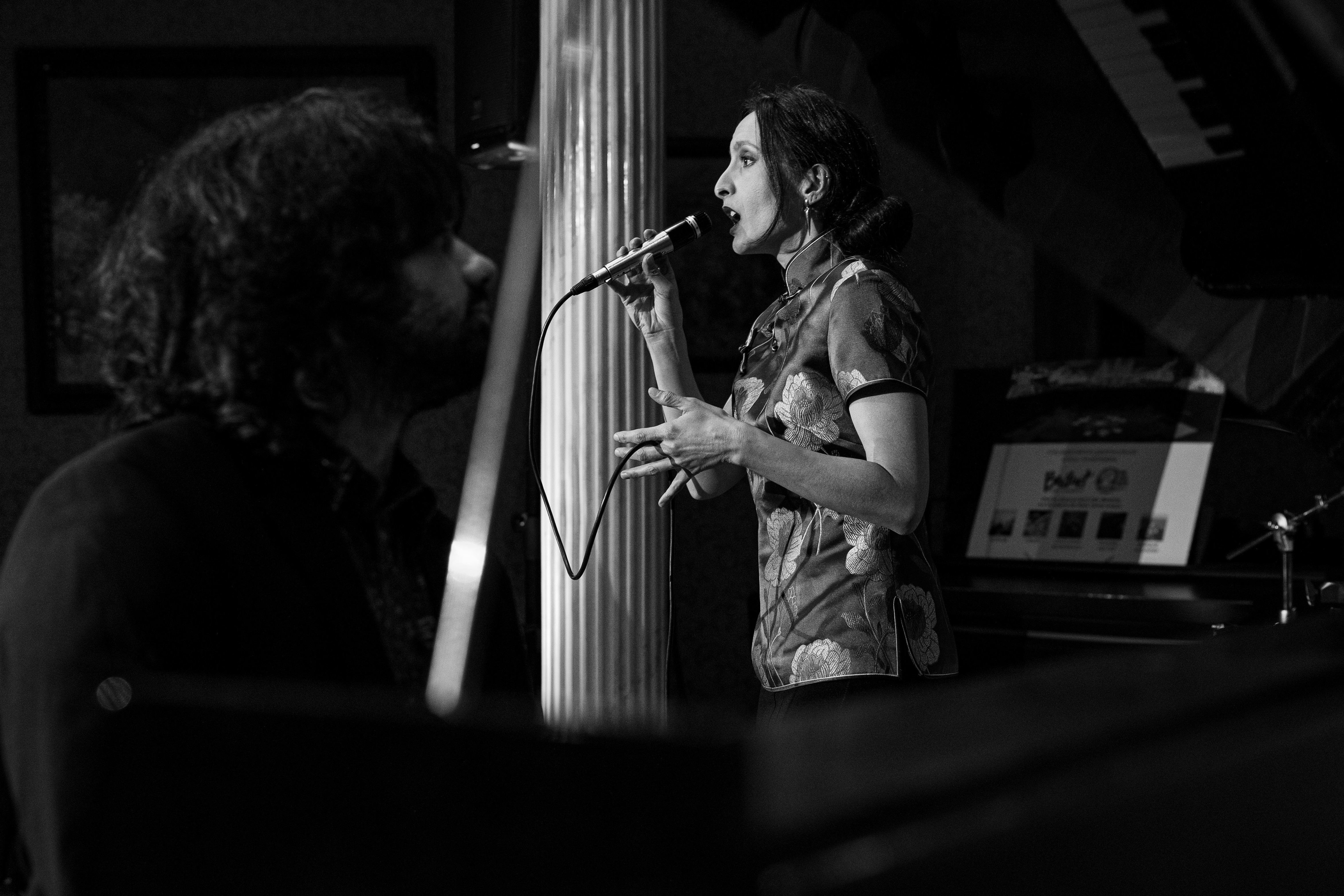 Una cantant actuant amb micròfon a l'escenari al costat d'un pianista durant un concert en blanc i negre del cicle Música a fons