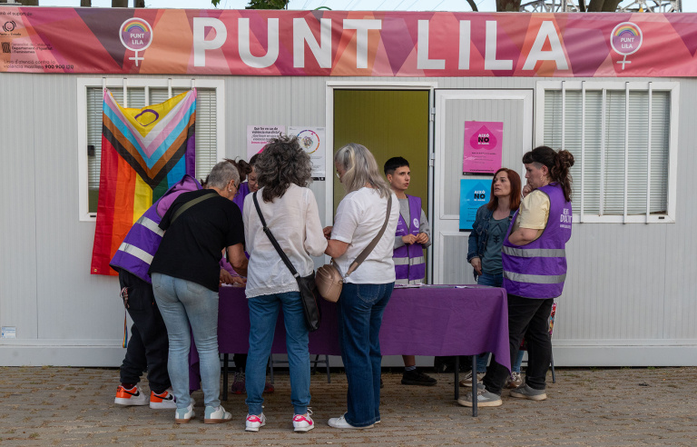 Persones interessades en un punt lila on hi ha una pancarta que ho posa i també una bandera LGTBI+
